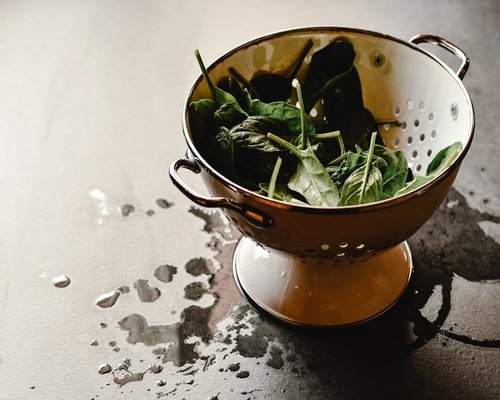 Fresh dark green spinach leaves with water droplets in a stone bowl